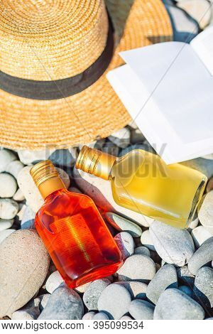 Beach Hat On Opened Book With Sunscreen And Shoes On Pebble Beach