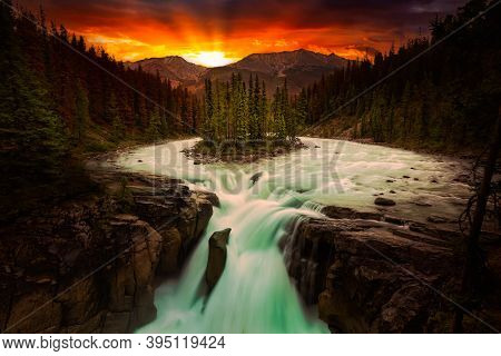 Glacier River And Waterfall Flowing In The Beautiful Canadian Rockies. Dramatic Colorful Sunset Sky 