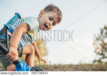 Caucasian Boy Is Climbing A Hill And Carry A Bike While Playing In A Field During A Walk