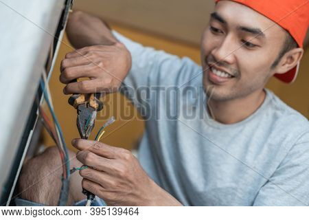 Close Up Of An Asian Electronics Worker Using Pliers To Fix A Washing Machine Cable That Broke