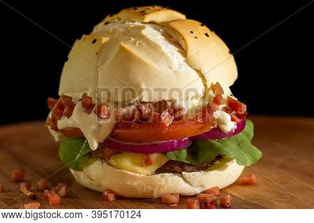 Close Up Of A Homemade Burger With Bacon And Salad A Chopping Wood Board, On Black Background