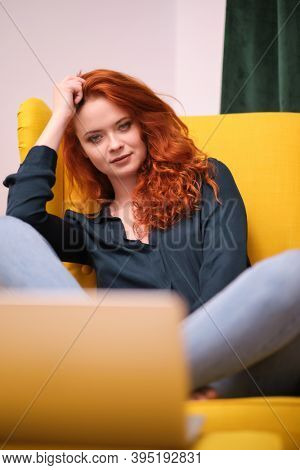 Nice beautiful lady with redhead curly hair work at the notebook sit down on the sofa at home - check on oline shops for cyber monday sales - technology woman concept for alternative office freelance