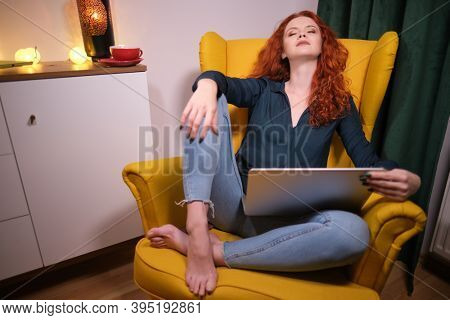 Nice beautiful lady with redhead curly hair work at the notebook sit down on the sofa at home - check on oline shops for cyber monday sales - technology woman concept for alternative office freelance
