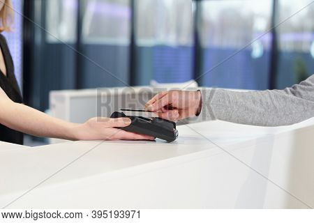 Young man holding smartphone over teminal held by shop assistant or administrator during contactless payment process in leisure center
