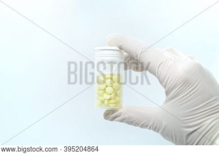 Close-up Of Gloved Hand Holding Transparent Pill Bottle On White Background. Concept: Medication Tre