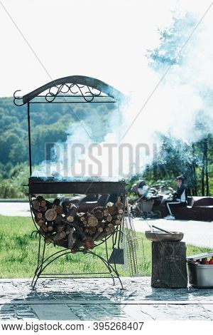 Flaming Log Wood In A Metal Outdoor Brazier With Ashes And Smoke In Rural Courtyard