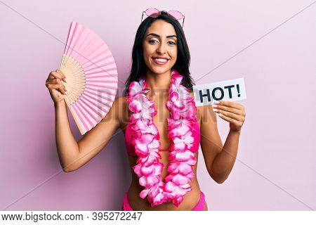 Beautiful hispanic woman wearing bikini and handfan holding hot word smiling with a happy and cool smile on face. showing teeth. 