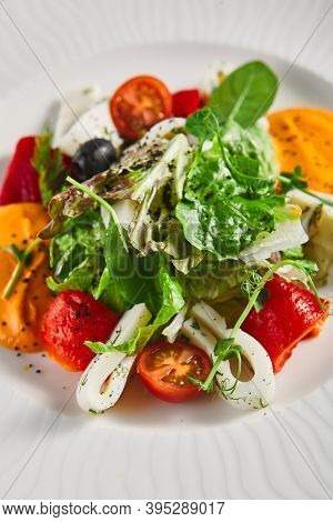 Roasted pepper salad with calamari and fresh greens. Rustic wooden table and grey textile