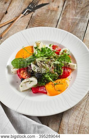 Roasted pepper salad with calamari and fresh greens. Rustic wooden table and grey textile