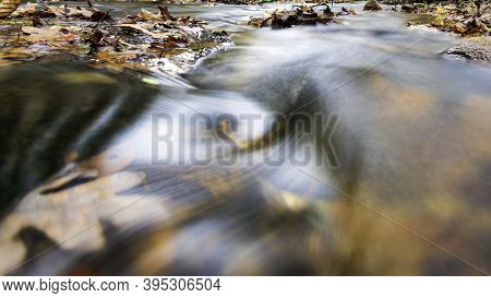 Abstract Nature Background Of Long Exposure Water Flowing Over Submurged Leaves In A Creek.