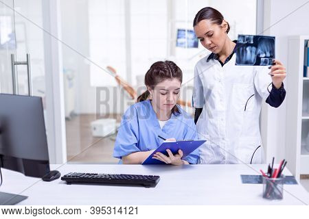 Dentist Nurse Taking Notes About Teeth Hygine While Doctor Is Holding X-ray. Stomatolog And Her Assi
