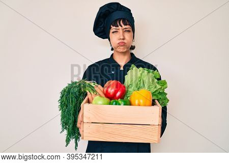 Beautiful brunettte woman chef holding fresh veggetables puffing cheeks with funny face. mouth inflated with air, catching air. 