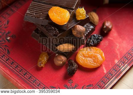 Close-up Of A Homemade Chocolate Bar With Raisins, Dried Apricot And Nuts On Red Book Background