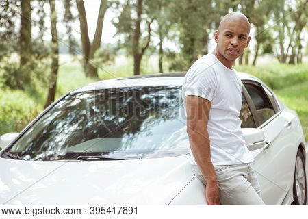 Attractive African Man Leaning On His Car On A Countryside Road, Looking Away Thoughtfully, Copy Spa