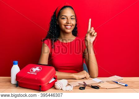 Young african american girl sitting on the table with first aid kit making cure smiling with an idea or question pointing finger up with happy face, number one 