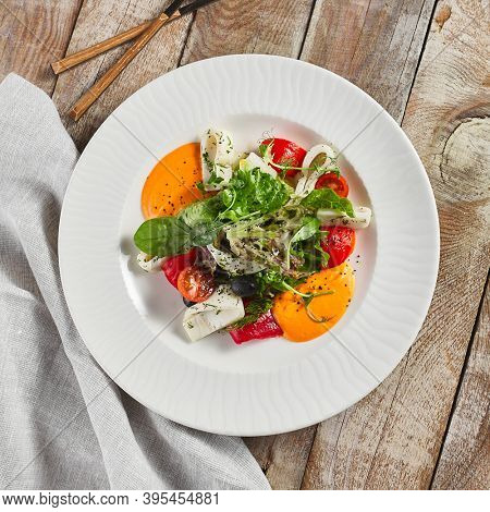 Roasted pepper salad with calamari and fresh greens. Rustic wooden table and grey textile
