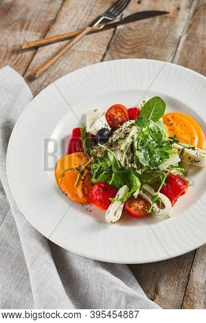 Roasted pepper salad with calamari and fresh greens. Rustic wooden table and grey textile