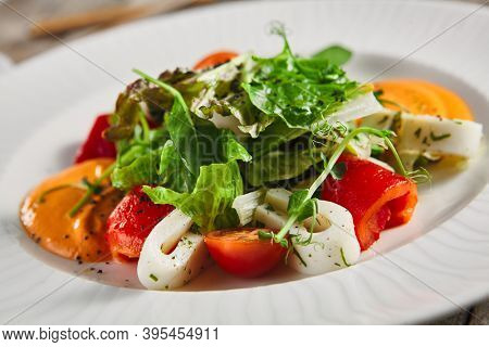 Roasted pepper salad with calamari and fresh greens. Rustic wooden table and grey textile