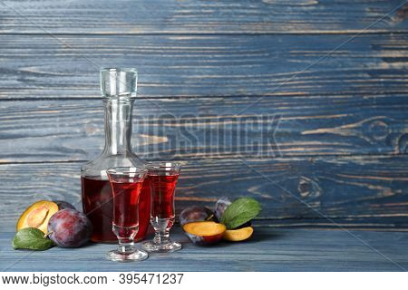 Delicious Plum Liquor And Ripe Fruits On Blue Wooden Table. Homemade Strong Alcoholic Beverage