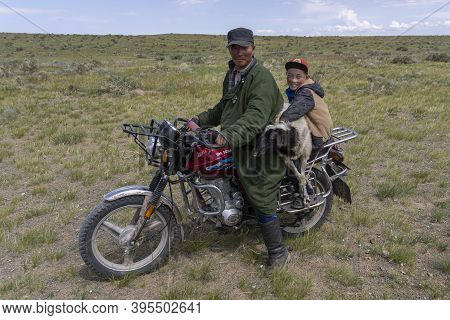 Olgii, Mongolia - August 7, 2019: Mongolian Man On A Motorbike With Boy And Sheep In The Steppe Of M