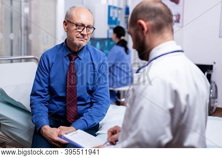 Senior Man Consulting With Doctor Sitting On Hospital Bed In Examination Room. Converstation With Me