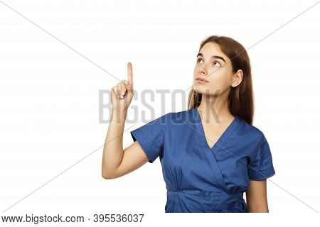 Young Beautiful Female Doctor In A Blue Surgical Gown Shows A Finger To The Side Isolated On A White