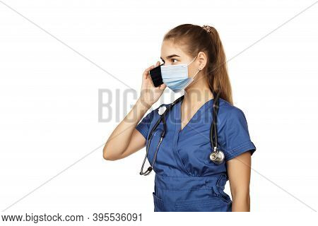 Young Beautiful Female Doctor In Blue Surgical Gown With Stethoscope Speaks On The Phone With A Pati