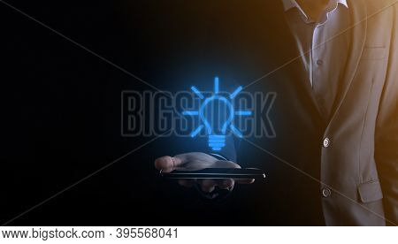 Businessman In A Suit With A Light Bulb In His Hands. Holds A Phone Smartphone Tablet Glowing Idea I