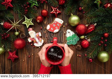 Woman Holding Hot Christmas Tea With Santas Sleigh And Deers Reflection Against Decorations On Woode