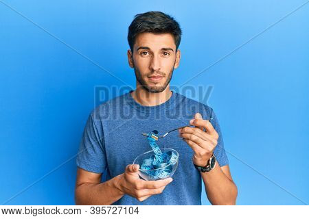 Young handsome man eating measure meter doing diet for weight loss relaxed with serious expression on face. simple and natural looking at the camera. 
