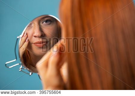 Redhaired Girl Reflecting In The Mirrror, On A Blue Background. Beauty Concept.