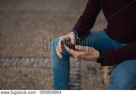 A Young Boy's Hands Using His Mobile Phone On The Street In A Red T-shirt.