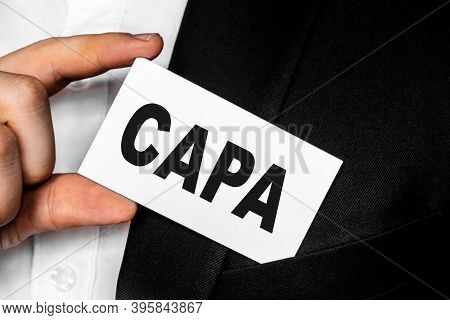 A Man In A Black Business Suit Lowers Or Removes From His Breast Pocket A White Business Card With T