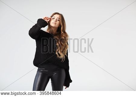 Pretty Young Woman In A Black Leather Leggings And Black Sweater Posing On A White Background. A Cau