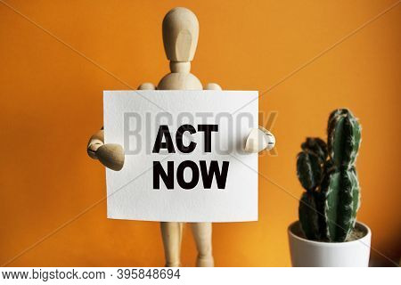 The Wooden Man Holds A White Sign With The Text Act Now In His Hands. The Content Of The Lettering H