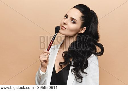 Portrait Of A Young Brunette Woman With Perfect Makeup Smiling And Kiping Makeup Brush Near Her Face