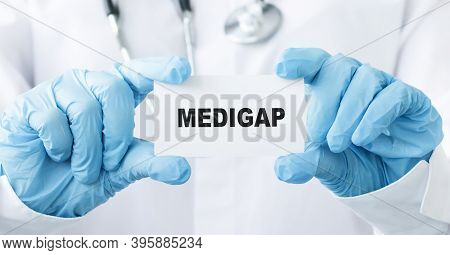 Doctor's Hands In Blue Gloves Shows The Word Medigap. Medical Concept.