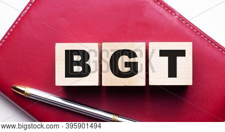 Bgt Is Made Up Of Wooden Cubes That Stand On A Burgundy Notebook Near The Pen. Business Concept