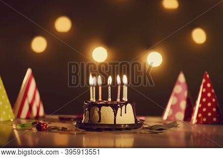 Birthday Drip Cake With Chocolate Ganache And Burning Candles On Table With Party Hats