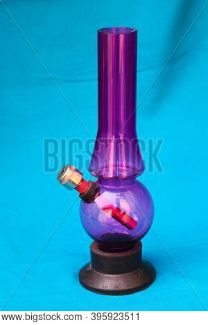 Glass Pipe Or Bong For Marijuana Smoking On A Blue Fabric Background