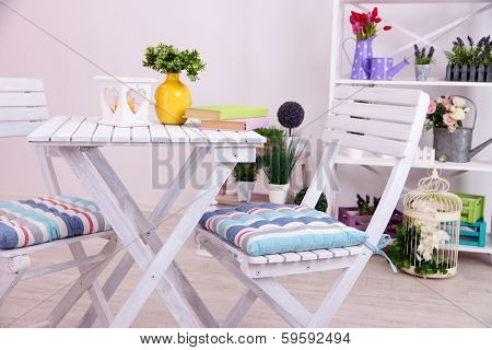 Garden chairs and table with flowers on shelves on white background