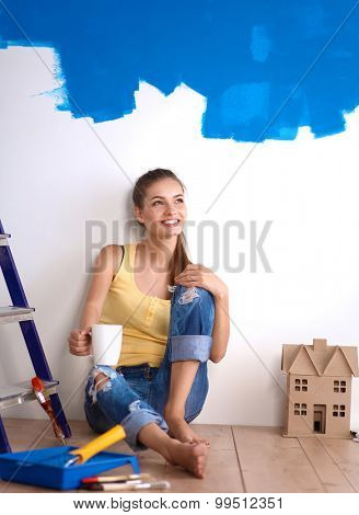 Portrait of female painter sitting on floor near wall after painting.