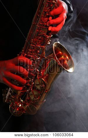 Musician in black shirt with sax on dark background, close up