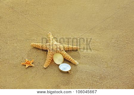 Compass with sea stars on sand beach background