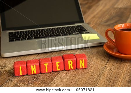 Intern written on a wooden cube in front of a laptop