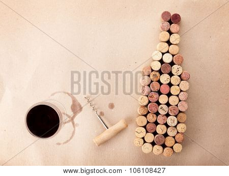 Wine bottle shaped corks, glass of wine and corkscrew over cardboard paper background. View from above with copy space
