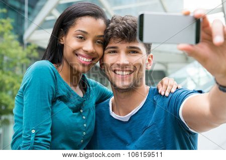 Closeup shot of young couple take selfie outdoor. Happy young man and woman smiling and photographing self in the city center. Happy young couple embracing and taking selfie with smartphone.