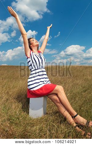 Young woman sitting while holding her hands up, outdoor picture.