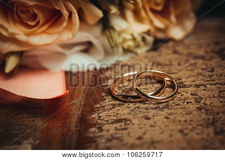Two wedding rings and a bouquet of orange and white roses.