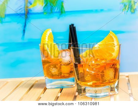 Two Glasses Of Spritz Aperitif Aperol Cocktail With Orange Slices And Ice Cubes On Blur Beach And Pa